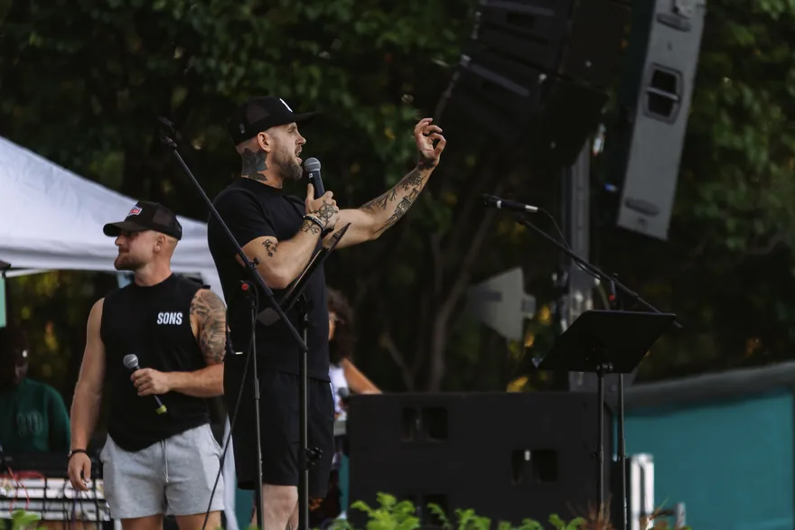 A Sons of Scripture speaker preaching into a microphone with one arm raised.